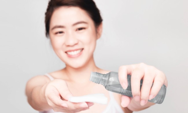 A woman holding up a bottle of face toner and a cotton pad to use.