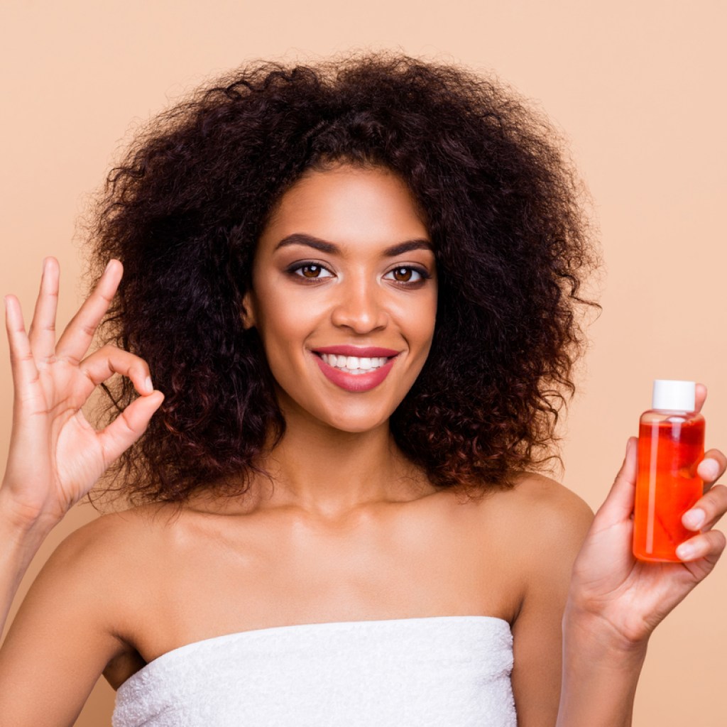 A woman holding a bottle of hair oil.