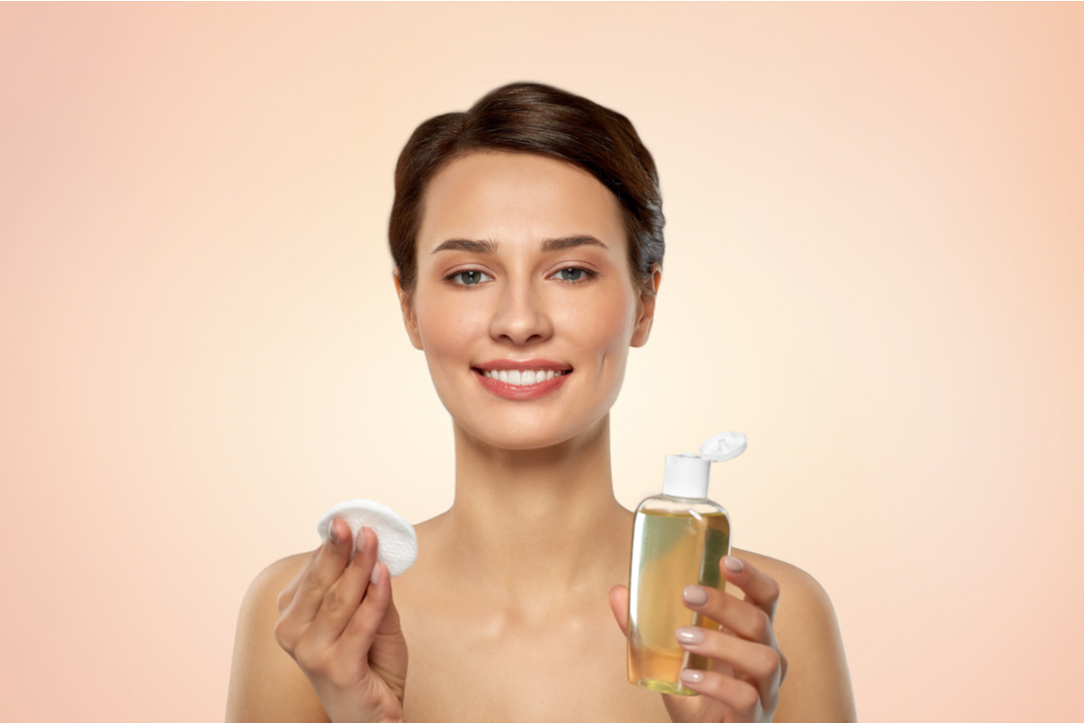 A woman holding up face toner and cotton pads.