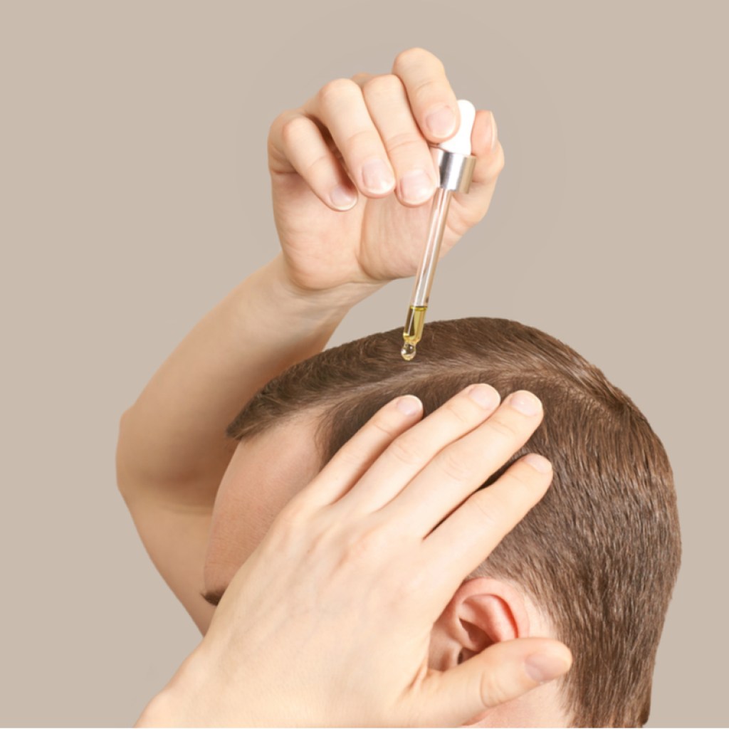 A man putting hair oil on his hairline.