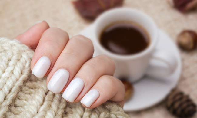 White painted nails with a coffee and leaves in the background.