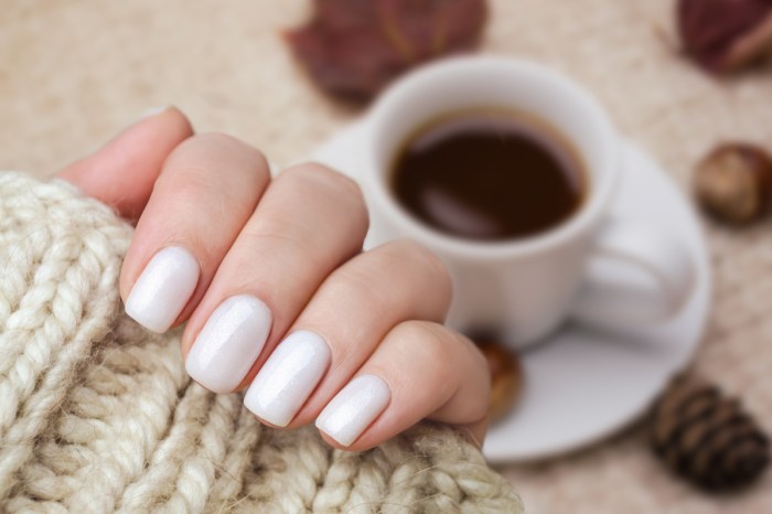 White painted nails with a coffee and leaves in the background.