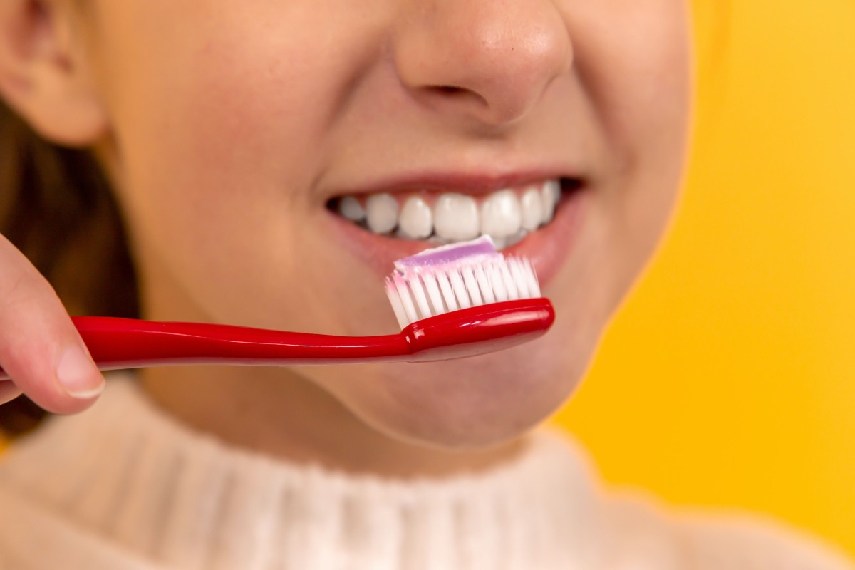 a closeup of a woman in a white sweater brushing her teeth