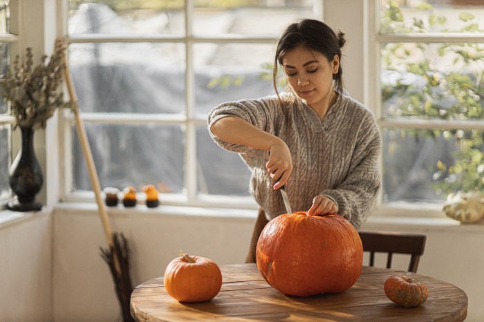 Woman cutting the top off of a pumpkin