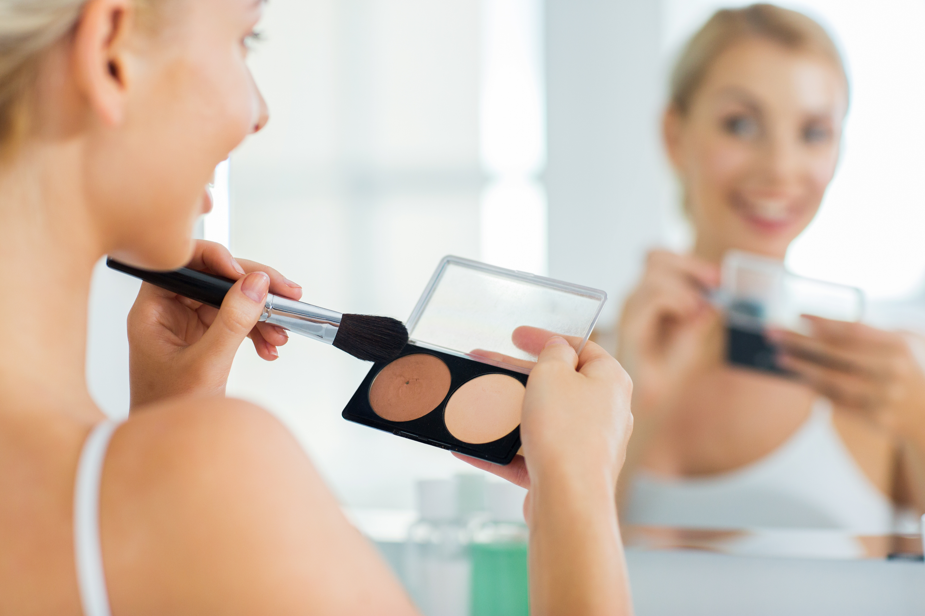 woman looking in mirror applying highlighter with brush