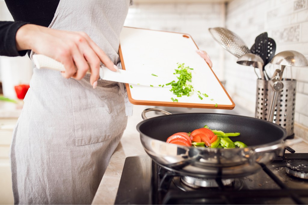 Closeup of woman's hands putting vegetables in pan