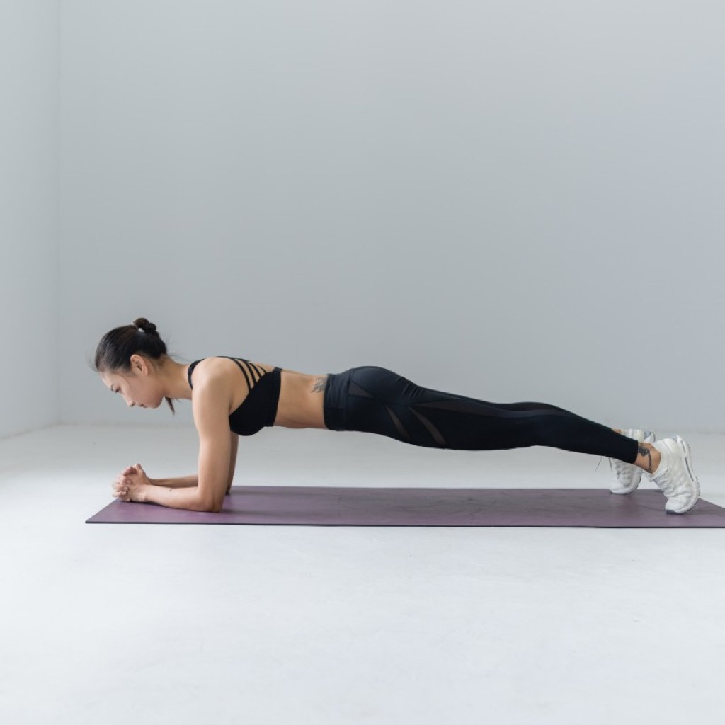 woman in a plank pose on a black mat in an all-white room