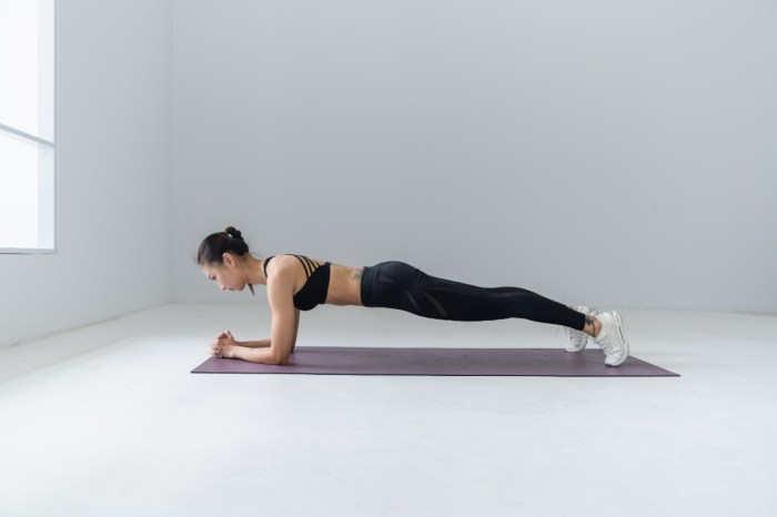 woman in a plank pose on a black mat in an all-white room