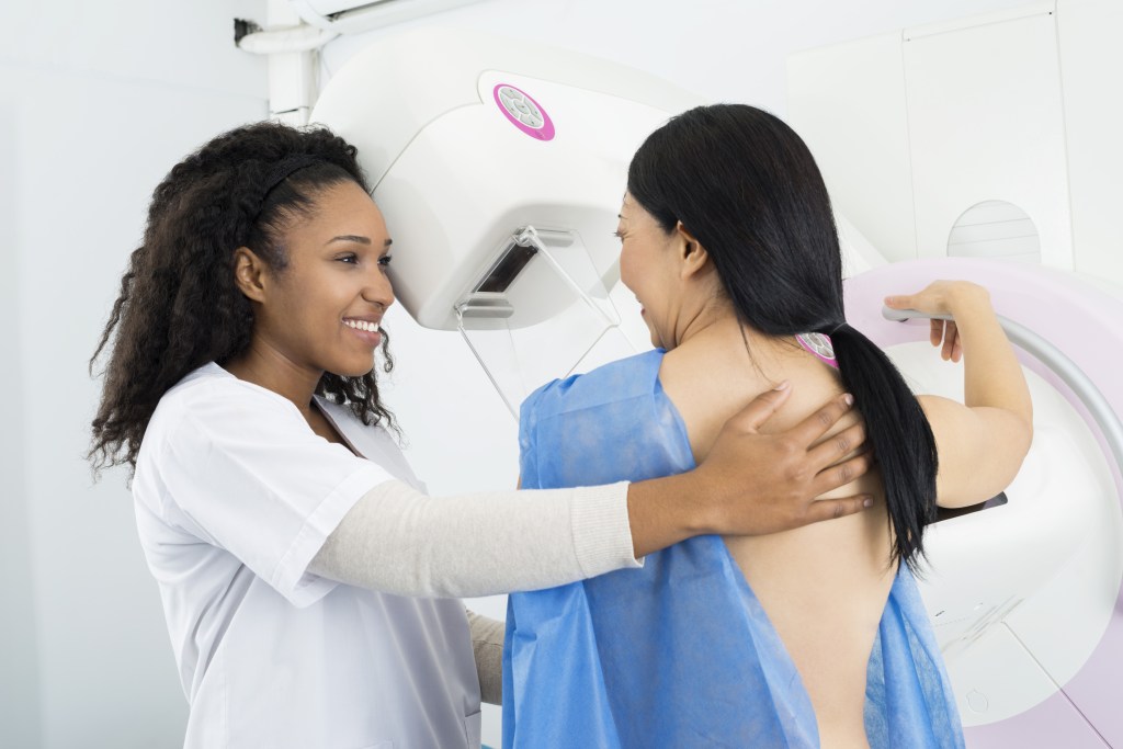 smiling woman undergoing mammogram with technician