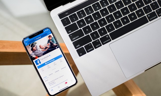 a phone with the facebook app pulled up, sitting next to a laptop on a desk