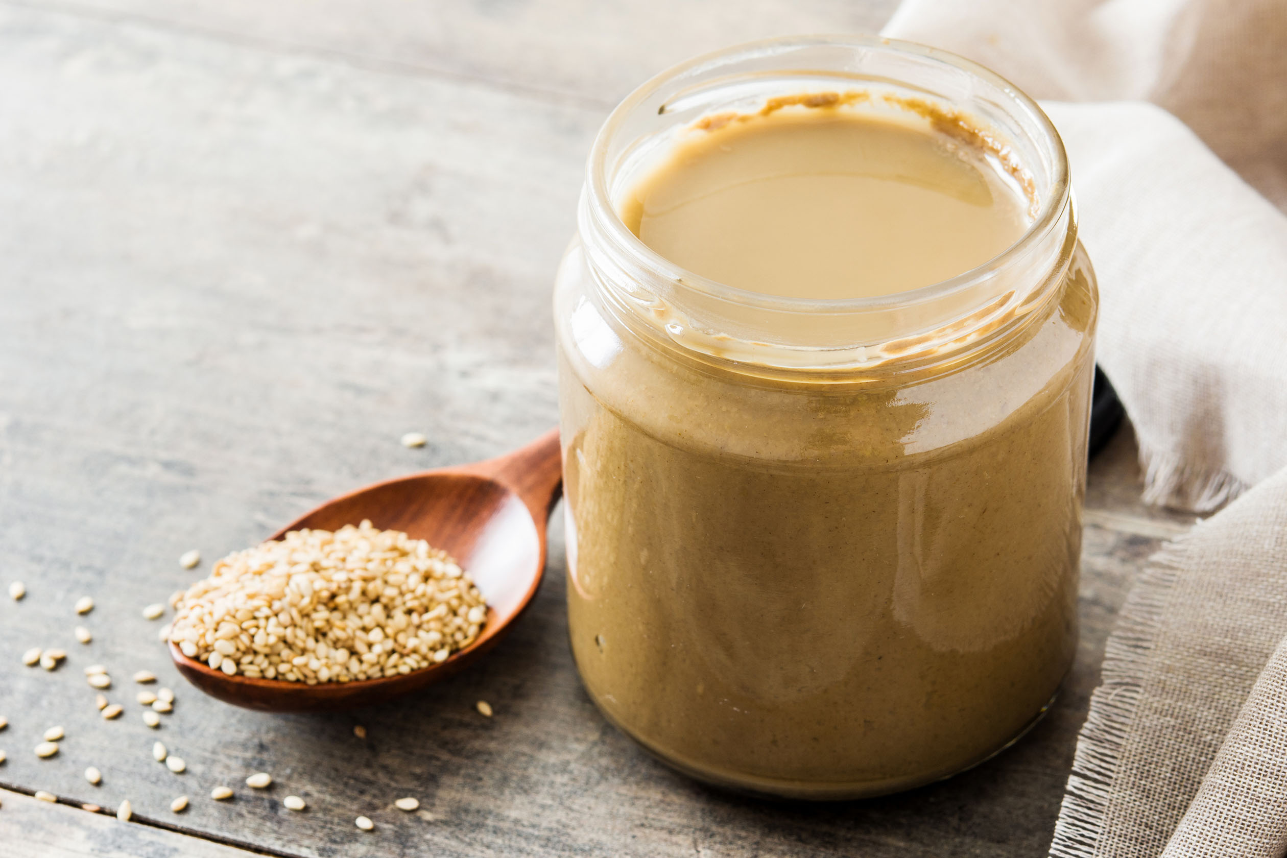 Jar of tahini and a spoonful of sesame seeds