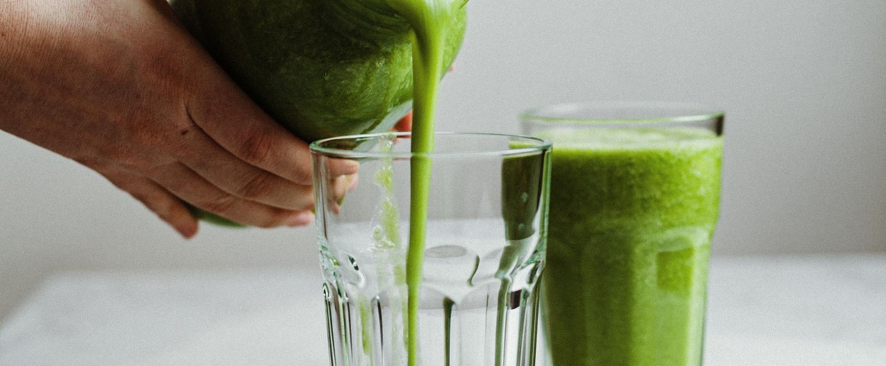 Person pouring green smoothie into cups
