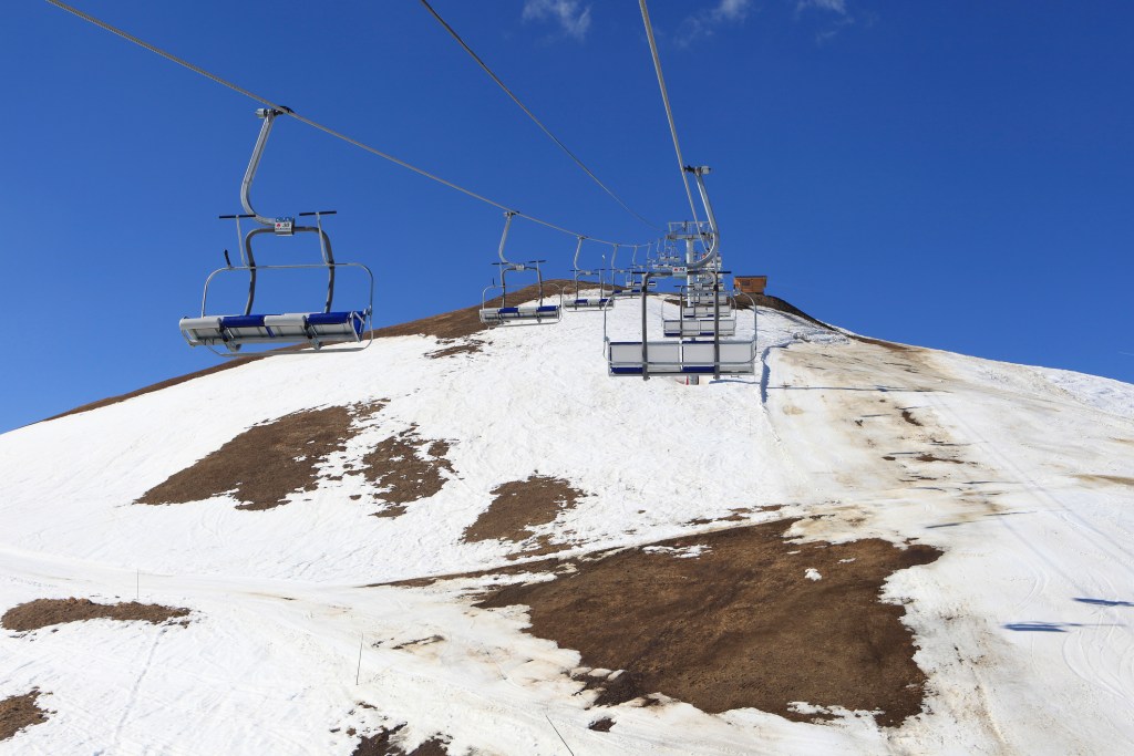 Empty skilifts over a hill with grass coming through the snow