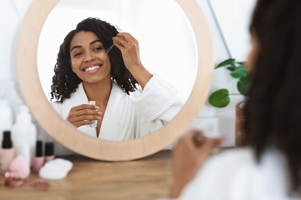 Woman looking in mirror applying facial oil