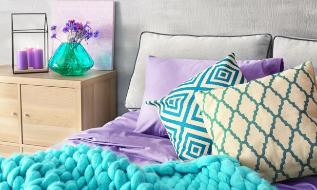 A well made bed with purple pillows and sheets and aqua accents