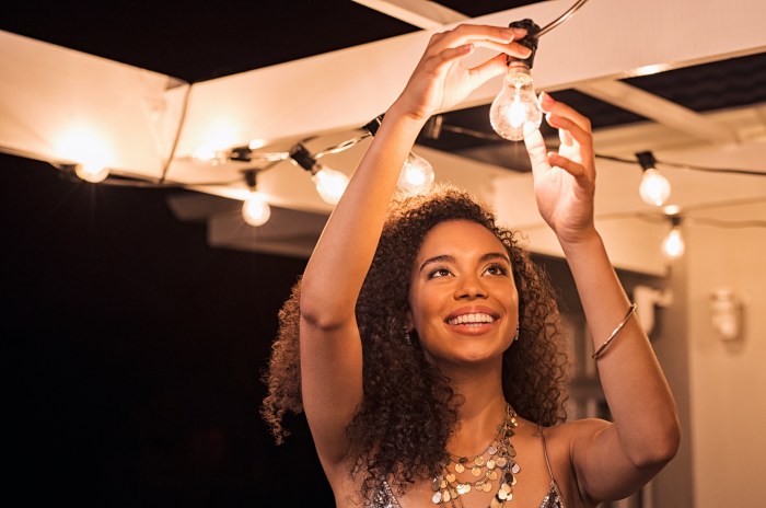 A woman with curly hair screws in a light bulb on a string of patio lights