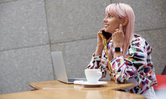 A woman with pink hair talks on the phone while working
